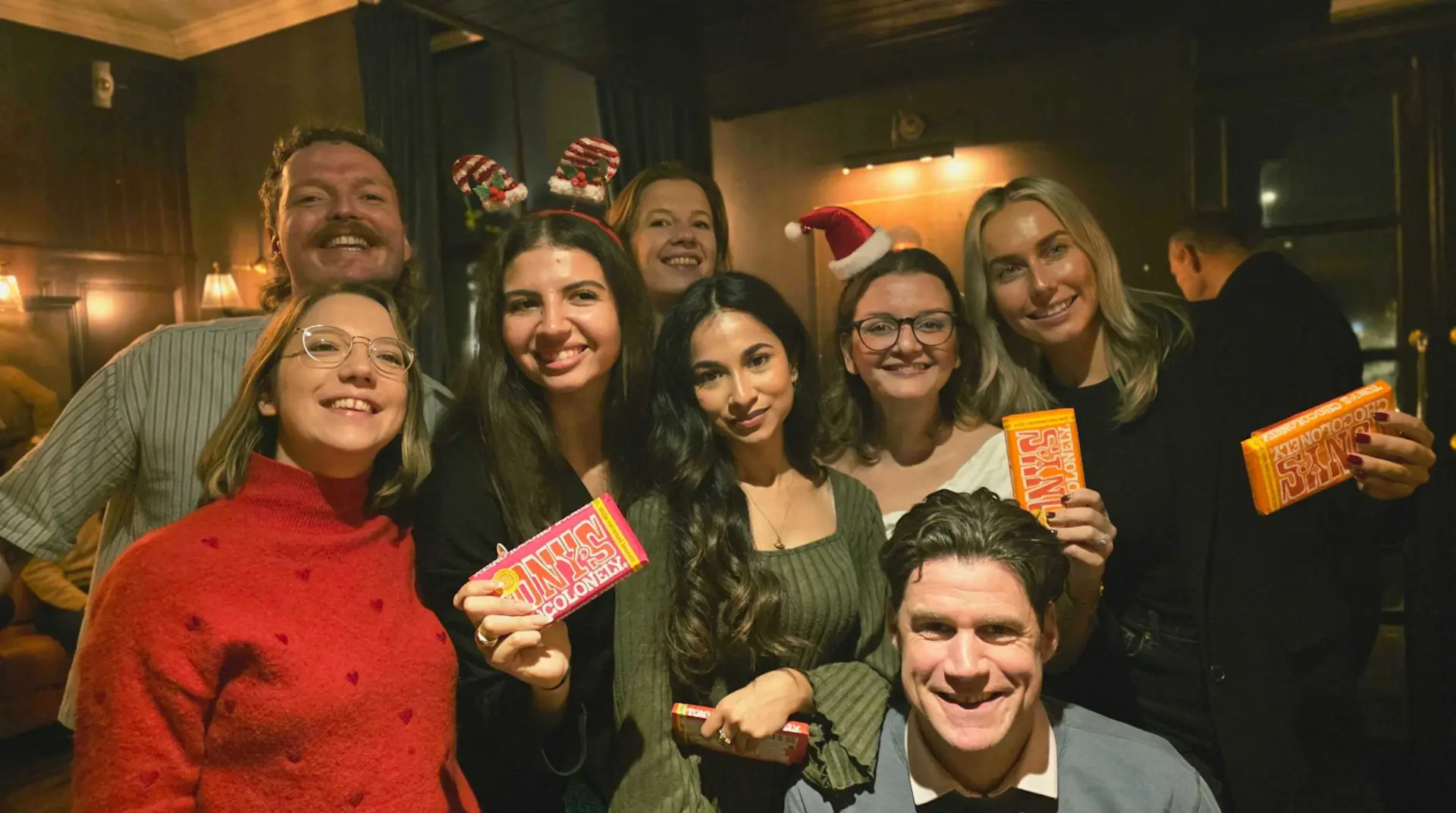 YOOBIC London teammates in festive headbands holding chocolate bars at the office Christmas party