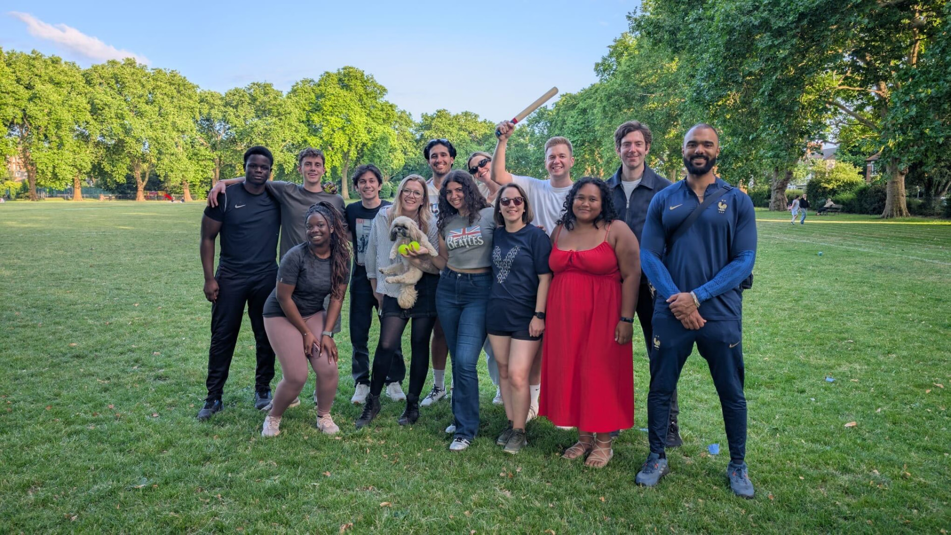YOOBIC London teammates playing rounders in a park, one holding a dog and one a bat